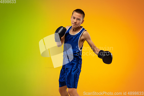 Image of Teenage boxer against gradient neon studio background in motion of kicking, boxing