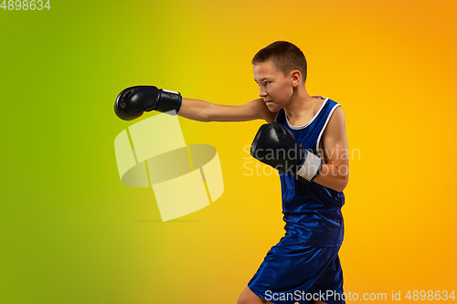 Image of Teenage boxer against gradient neon studio background in motion of kicking, boxing