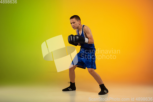 Image of Teenage boxer against gradient neon studio background in motion of kicking, boxing