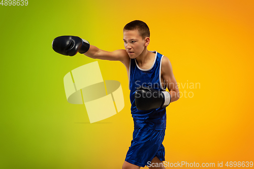 Image of Teenage boxer against gradient neon studio background in motion of kicking, boxing