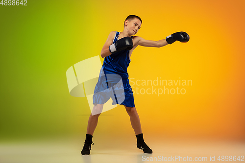 Image of Teenage boxer against gradient neon studio background in motion of kicking, boxing