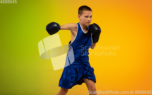 Image of Teenage boxer against gradient neon studio background in motion of kicking, boxing