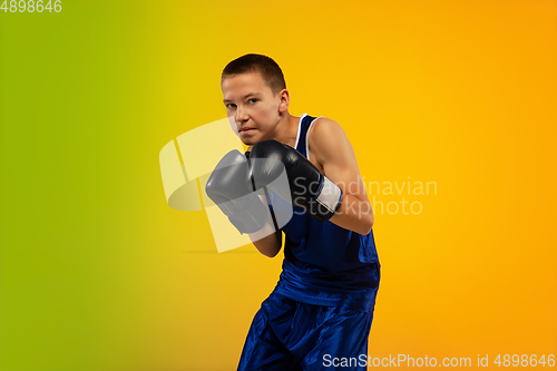 Image of Teenage boxer against gradient neon studio background in motion of kicking, boxing