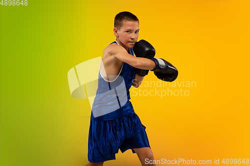 Image of Teenage boxer against gradient neon studio background in motion of kicking, boxing