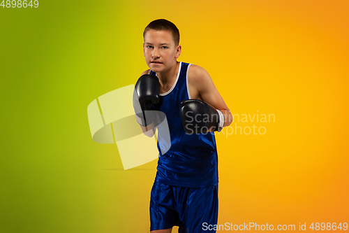 Image of Teenage boxer against gradient neon studio background in motion of kicking, boxing