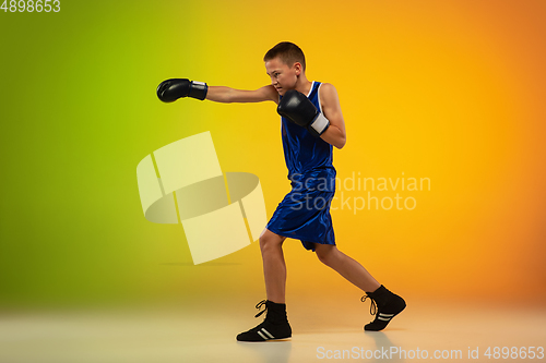 Image of Teenage boxer against gradient neon studio background in motion of kicking, boxing