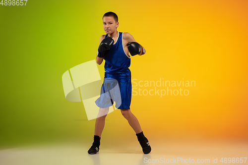 Image of Teenage boxer against gradient neon studio background in motion of kicking, boxing