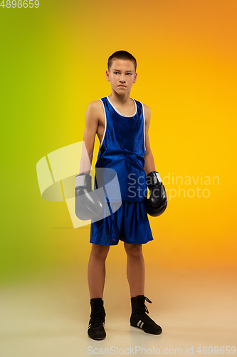 Image of Teenage boxer against gradient neon studio background in motion of kicking, boxing