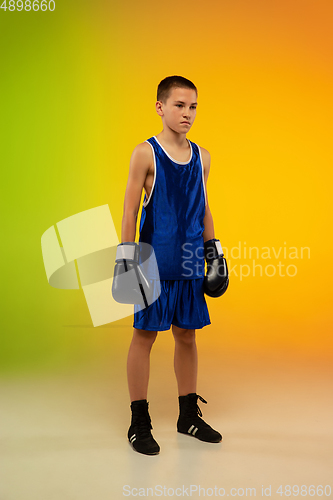 Image of Teenage boxer against gradient neon studio background in motion of kicking, boxing