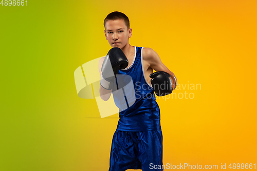 Image of Teenage boxer against gradient neon studio background in motion of kicking, boxing