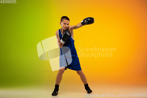 Image of Teenage boxer against gradient neon studio background in motion of kicking, boxing