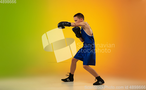 Image of Teenage boxer against gradient neon studio background in motion of kicking, boxing