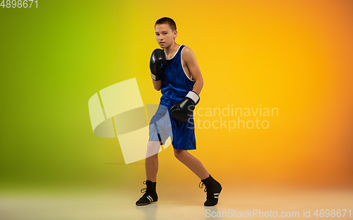 Image of Teenage boxer against gradient neon studio background in motion of kicking, boxing