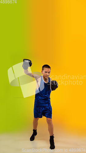 Image of Teenage boxer against gradient neon studio background in motion of kicking, boxing