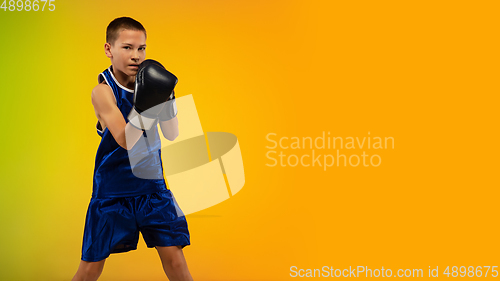 Image of Teenage boxer against gradient neon studio background in motion of kicking, boxing