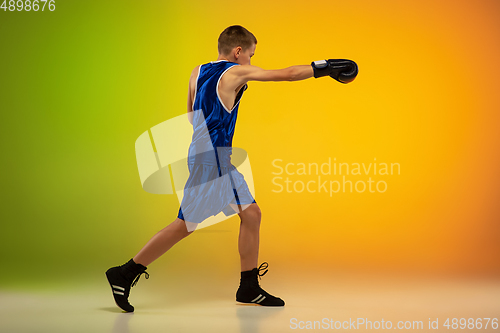 Image of Teenage boxer against gradient neon studio background in motion of kicking, boxing