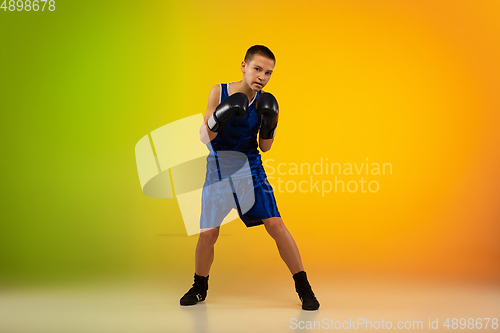 Image of Teenage boxer against gradient neon studio background in motion of kicking, boxing