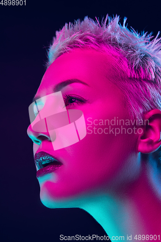 Image of Portrait of female fashion model in neon light on dark studio background.