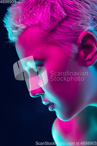Image of Portrait of female fashion model in neon light on dark studio background.