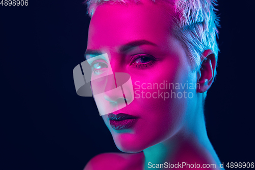 Image of Portrait of female fashion model in neon light on dark studio background.