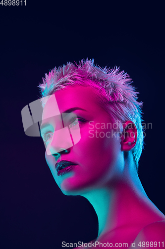 Image of Portrait of female fashion model in neon light on dark studio background.