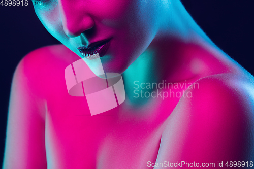 Image of Portrait of female fashion model in neon light on dark studio background.