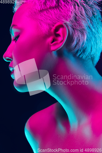 Image of Portrait of female fashion model in neon light on dark studio background.