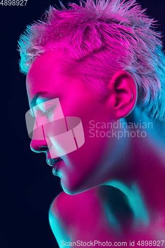 Image of Portrait of female fashion model in neon light on dark studio background.