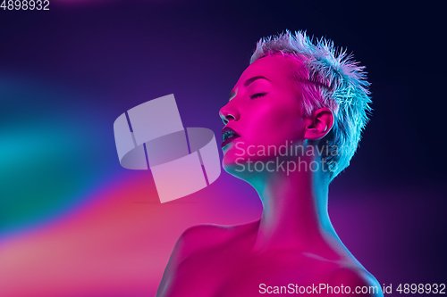 Image of Portrait of female fashion model in neon light on dark studio background.