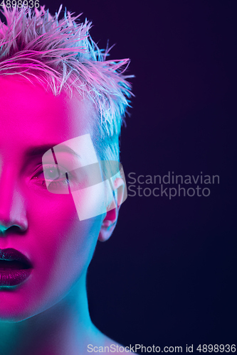 Image of Portrait of female fashion model in neon light on dark studio background.