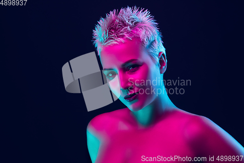 Image of Portrait of female fashion model in neon light on dark studio background.