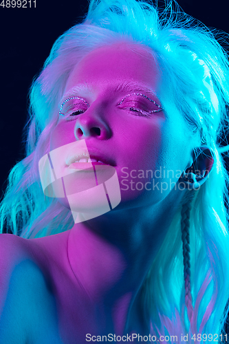 Image of Portrait of beautiful albino girl isolated on dark studio background in neon light