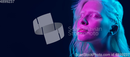 Image of Portrait of beautiful albino girl isolated on dark studio background in neon light
