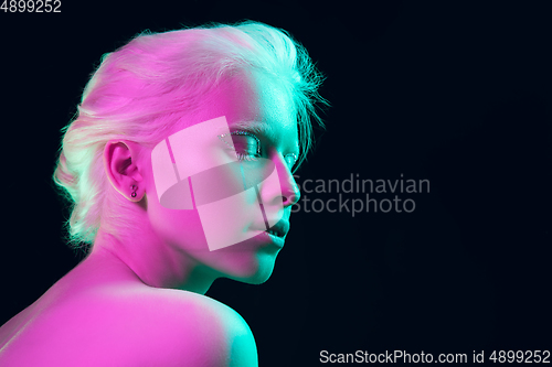 Image of Portrait of beautiful albino girl isolated on dark studio background in neon light