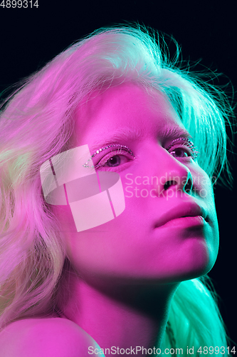 Image of Portrait of beautiful albino girl isolated on dark studio background in neon light