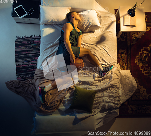 Image of Top view of young professional basketball player sleeping at his bedroom in sportwear with ball