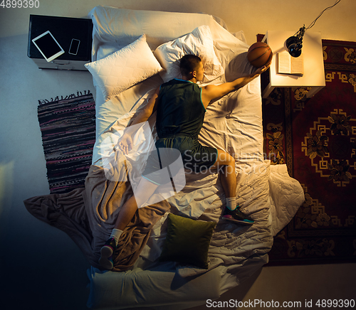 Image of Top view of young professional basketball player sleeping at his bedroom in sportwear with ball