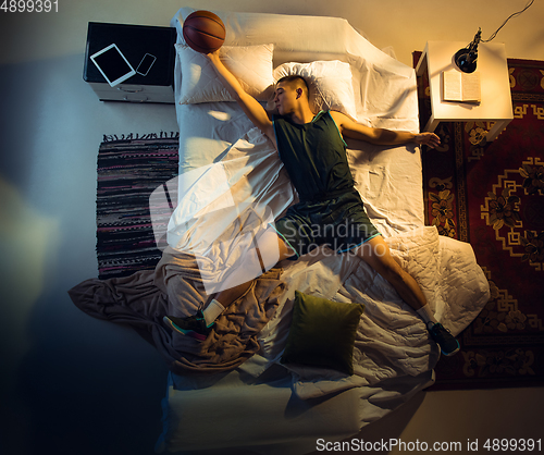 Image of Top view of young professional basketball player sleeping at his bedroom in sportwear with ball