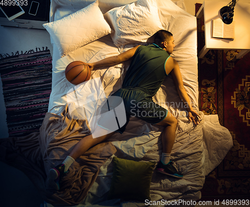 Image of Top view of young professional basketball player sleeping at his bedroom in sportwear with ball