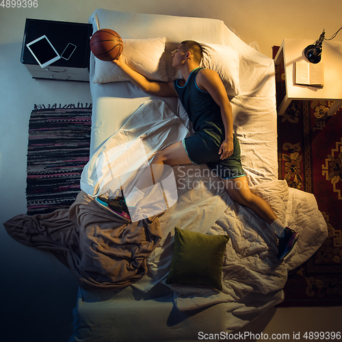 Image of Top view of young professional basketball player sleeping at his bedroom in sportwear with ball