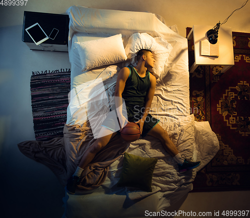 Image of Top view of young professional basketball player sleeping at his bedroom in sportwear with ball