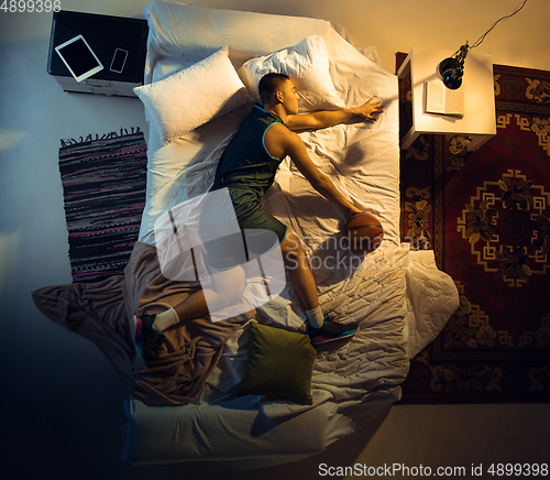 Image of Top view of young professional basketball player sleeping at his bedroom in sportwear with ball