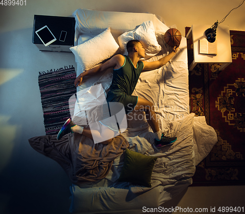 Image of Top view of young professional basketball player sleeping at his bedroom in sportwear with ball