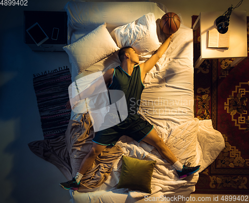 Image of Top view of young professional basketball player sleeping at his bedroom in sportwear with ball