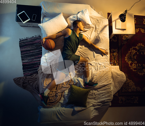 Image of Top view of young professional basketball player sleeping at his bedroom in sportwear with ball