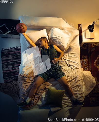 Image of Top view of young professional basketball player sleeping at his bedroom in sportwear with ball