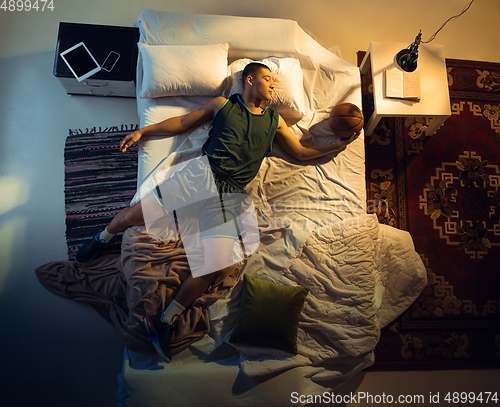 Image of Top view of young professional basketball player sleeping at his bedroom in sportwear with ball