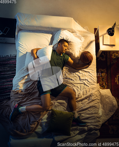 Image of Top view of young professional basketball player sleeping at his bedroom in sportwear with ball