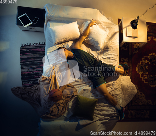 Image of Top view of young professional basketball player sleeping at his bedroom in sportwear with ball