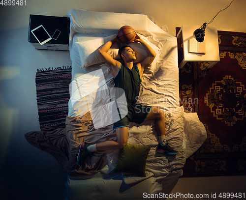 Image of Top view of young professional basketball player sleeping at his bedroom in sportwear with ball